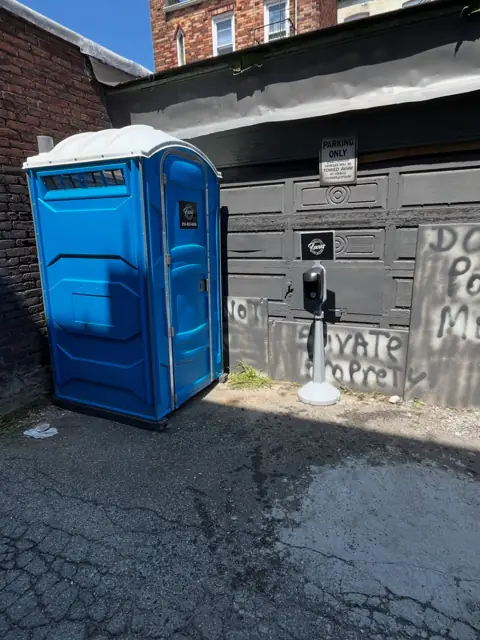 Blue porta potty beside a building
