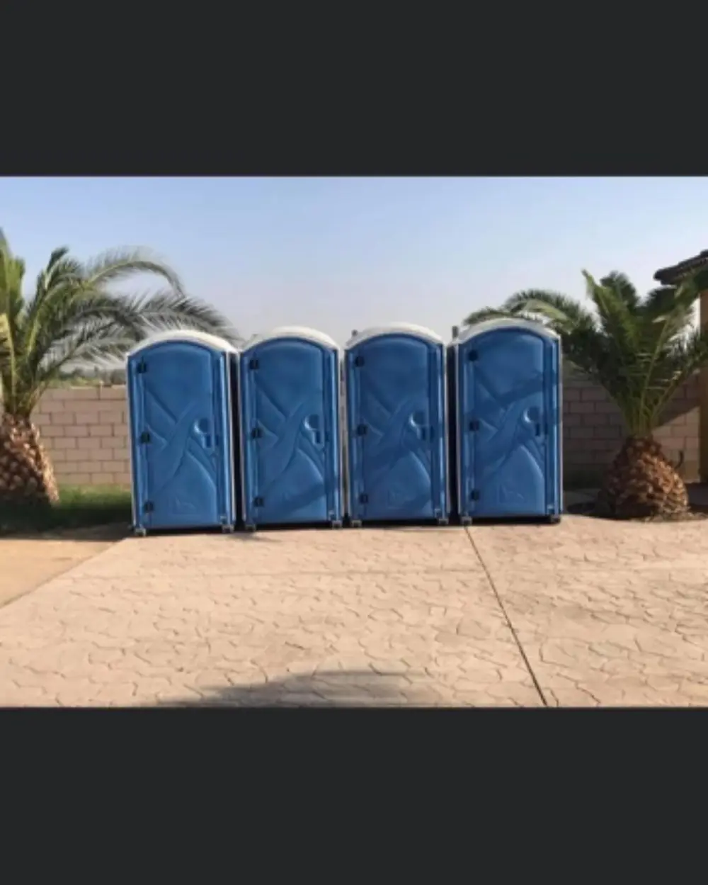 Four blue porta potties lined up on pavers