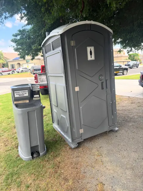Gray porta potty with a hand-wash station on grass