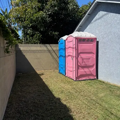 Pink and blue porta potties along a backyard fence
