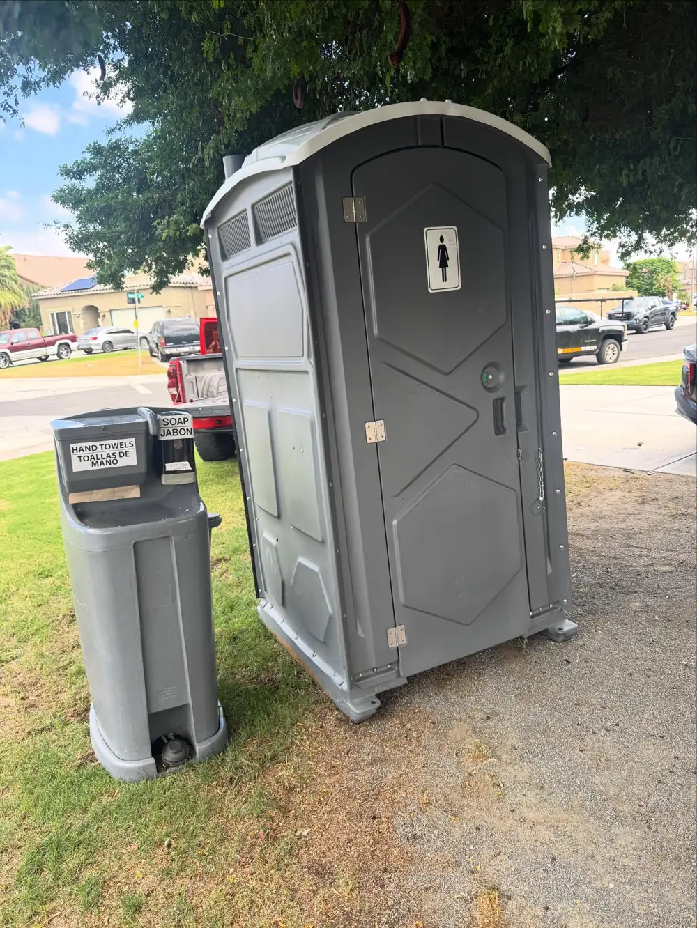 Gray porta potty with a hand-wash station on grass
