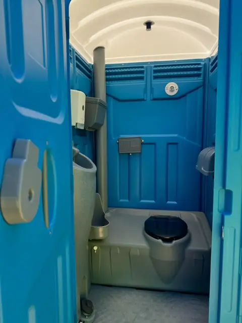 Inside a standard porta potty showing the seat, urinal and sanitizer